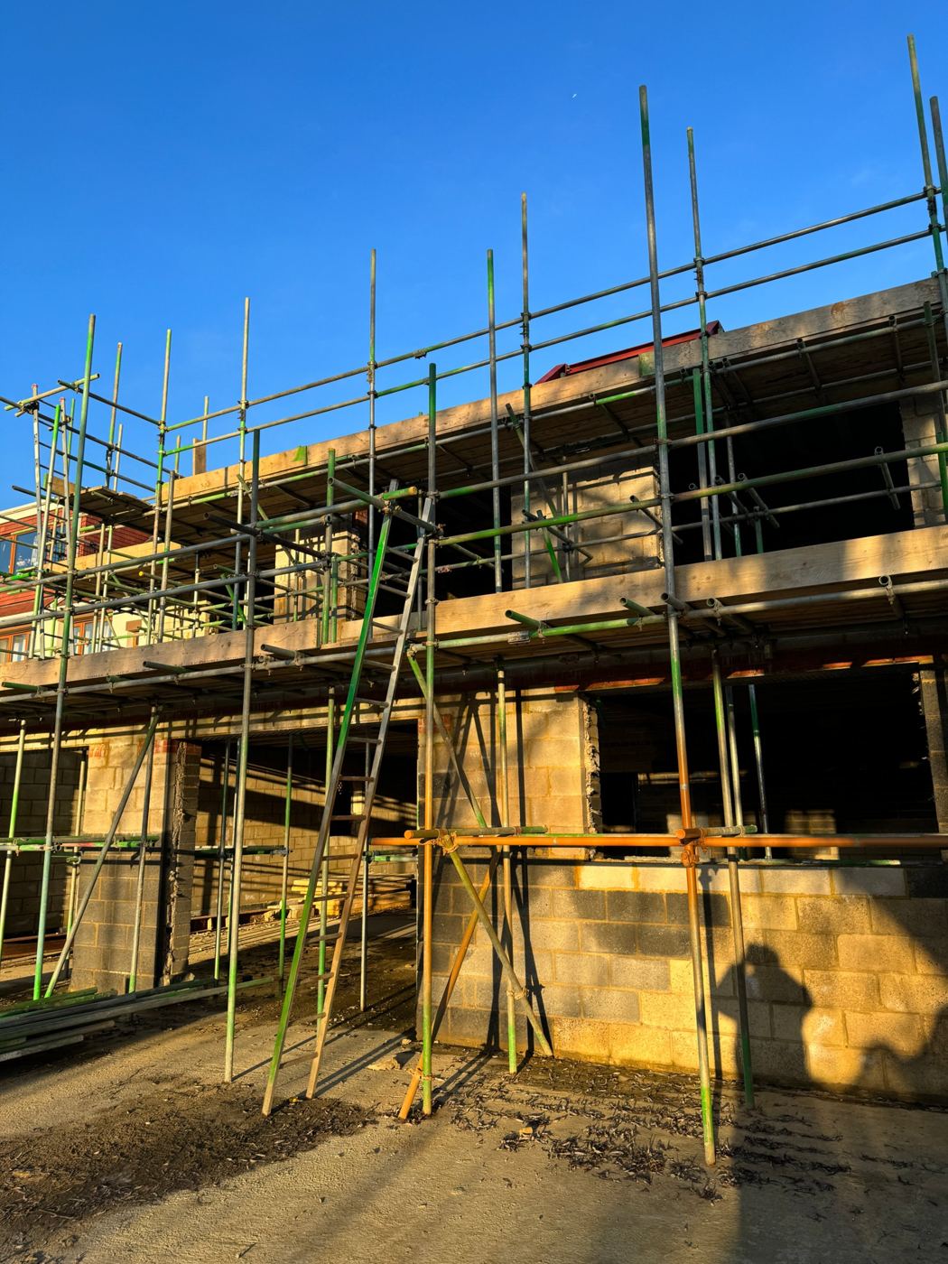 Two-storey blockwork shell under scaffold in low evening sun